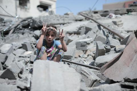 Child holding up peace hand sign amidst rubble in Gaza.